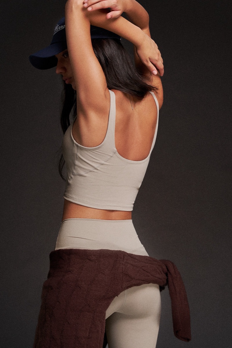 Woman in a navy cap, sage tank top and beige leggings